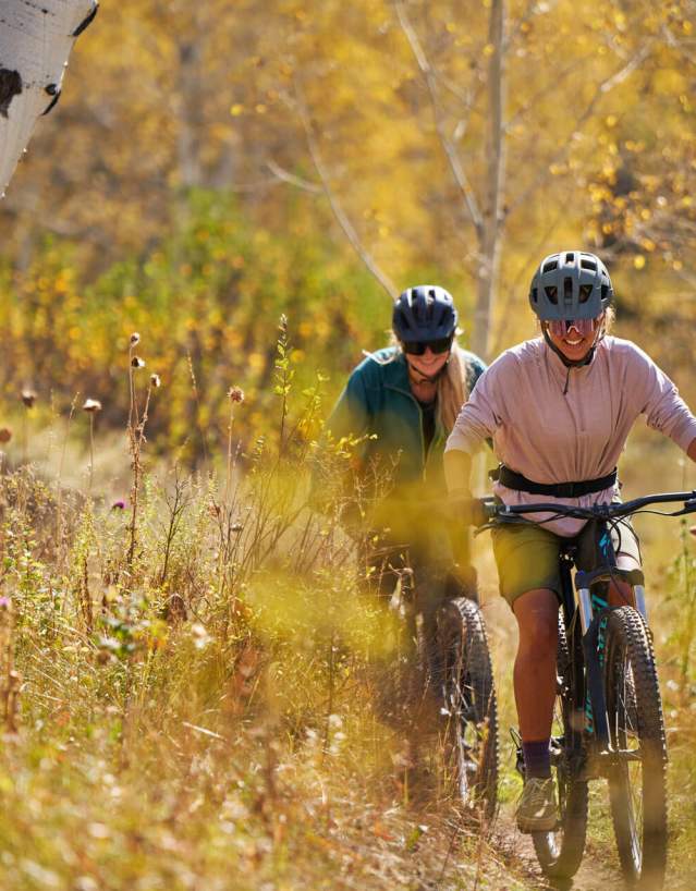Mountain bikers riding along a scenic trail surrounded by vibrant fall foliage in Wyoming.