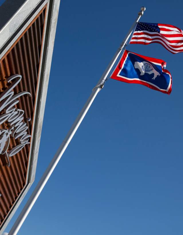 American and Wyoming state flags fly outside the Southeast Wyoming Welcome Center in Wyoming beneath a clear blue sky.