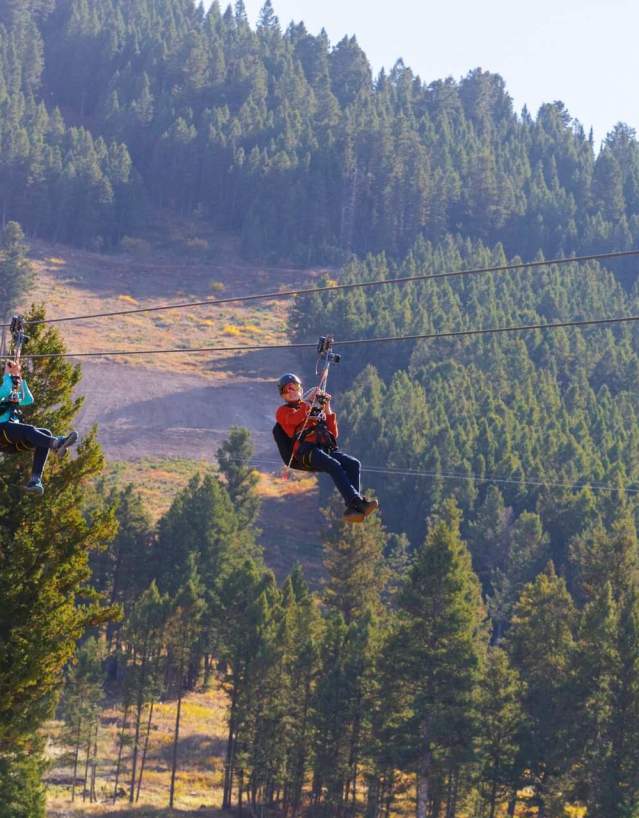 Riders soaring on a zipline over snowy landscapes at Snow King Mountain in Wyoming.