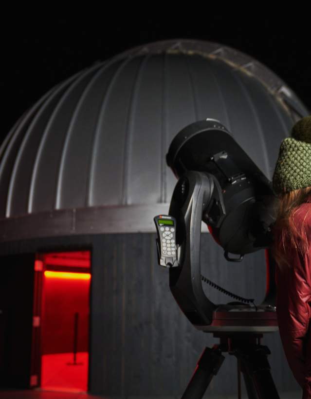 Snow King Observatory in Jackson, Wyoming, featuring the modern, geometric building set against a dark sky filled with visible stars and a portion of the Teton mountain range. Open year round.