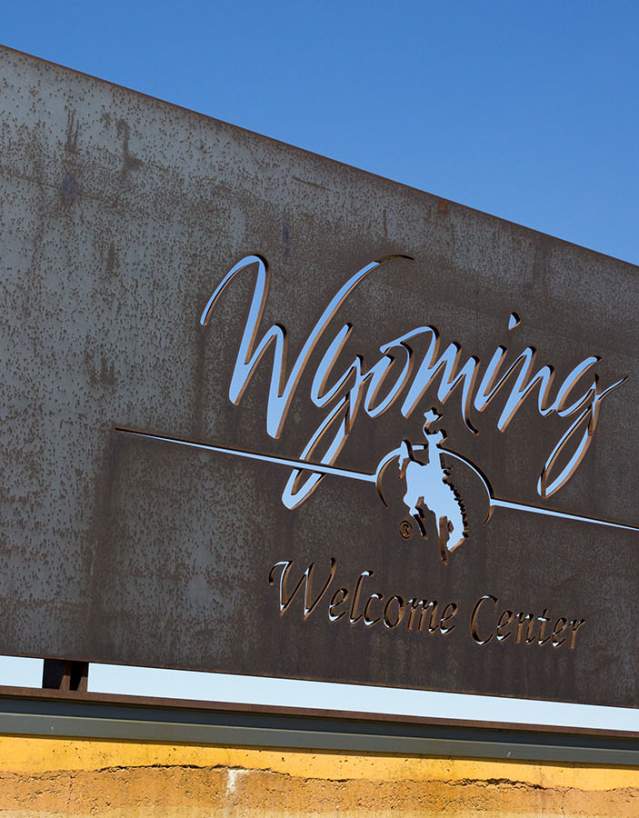 Bronze Wyoming welcome center sign set against clear blue sky.