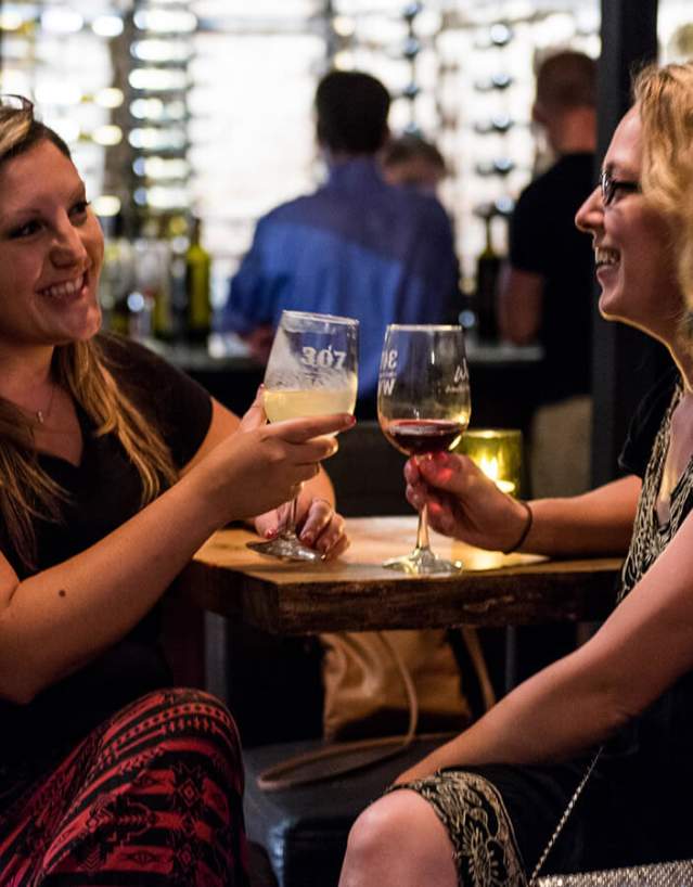 Two people sitting at a table clinking wine glasses.