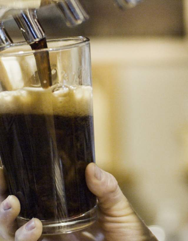 Hands pouring a dark craft beer from tap.