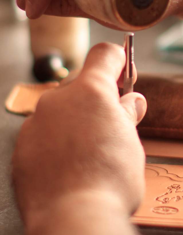 Hands crafting leather with tools.