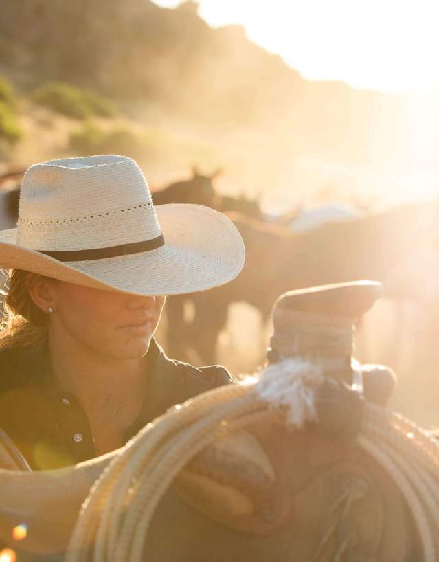 Cowgirl next to a horse and saddle at sunset.