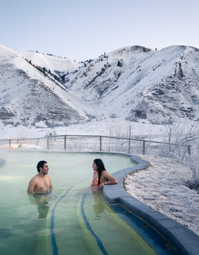 Steam rising from a natural hot spring with people soaking surrounded by snowy landscapes at Astoria Hot Springs Park in Wyoming.