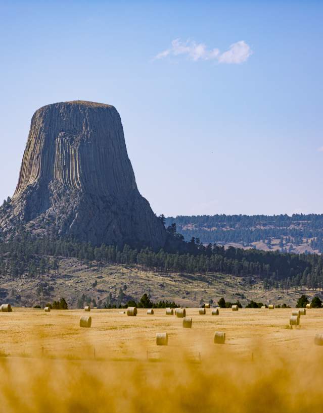 Looming geological tower over amber field of hay bales