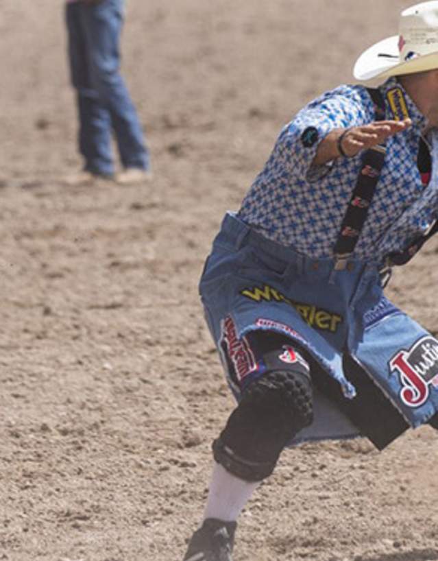 Rodeo clown facing off with a bull in a rodeo arena.