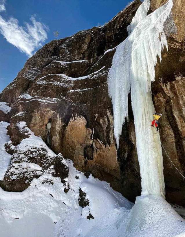 Ice climber scaling frozen waterfall against mountain.