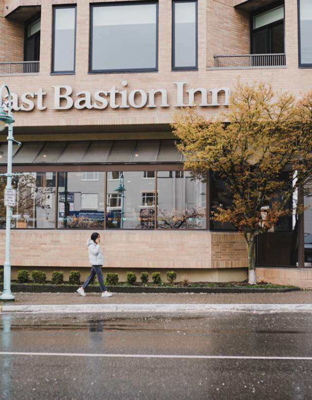 A person walks past The Coast Bastion Inn on a rainy day, with wet pavement and trees lining the street.