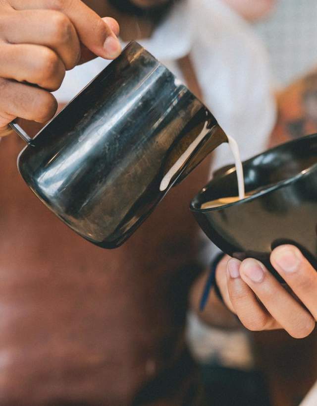 A Barista artfully pours steamed milk into a fresh cappuccino at Pax & Beneficia Coffee
