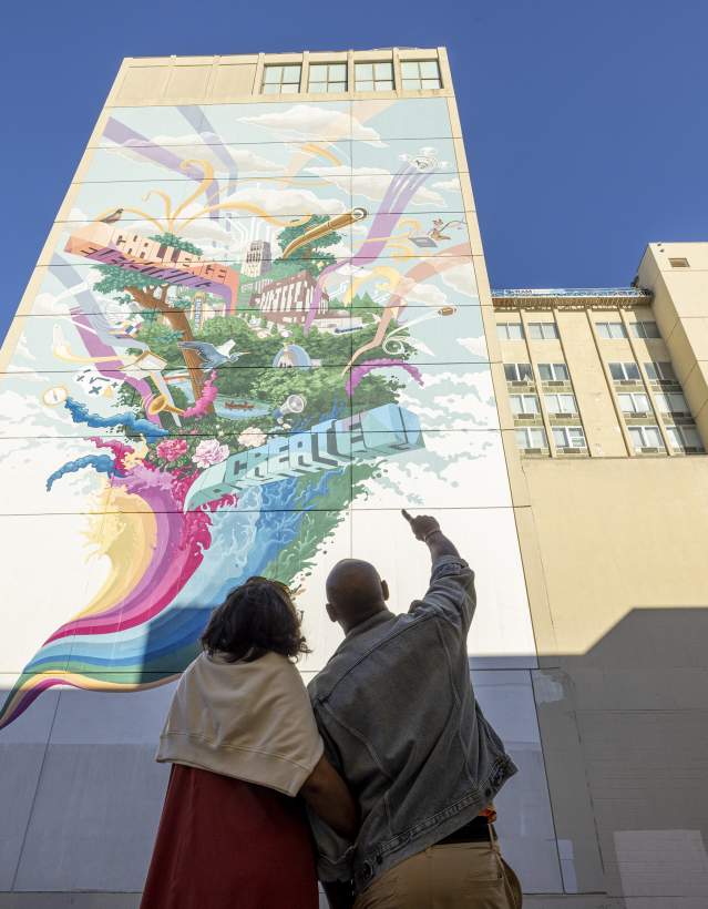 Couple pointing upward at tall, colorful mural