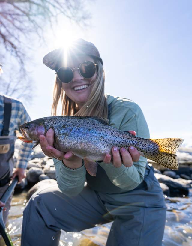 Woman holding a trout while fly fishing with a man.
