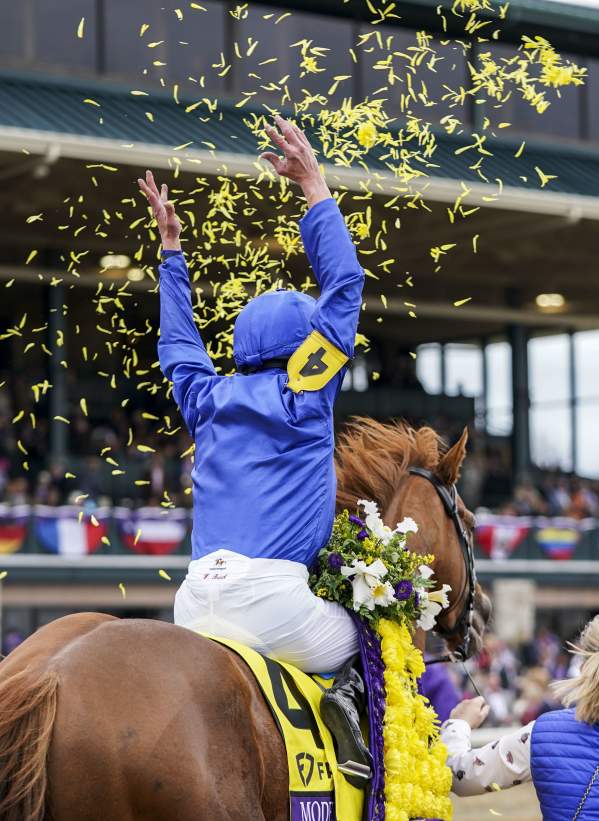 A jockey in blue and yellow silks celebrating a win atop a thoroughbred horse amidst yellow confetti at Keeneland.