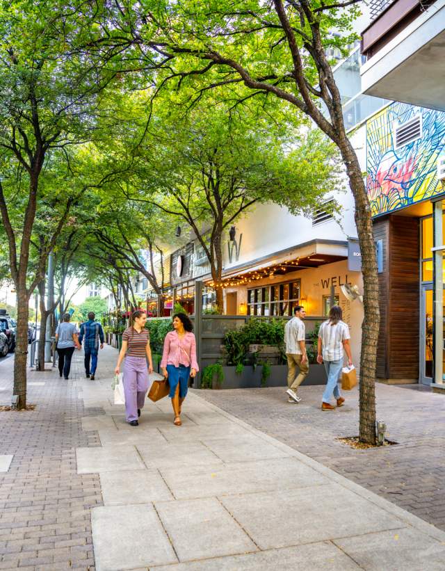 People walking on the sidewalk through the 2ND Street District chatting while holding shopping bags.
