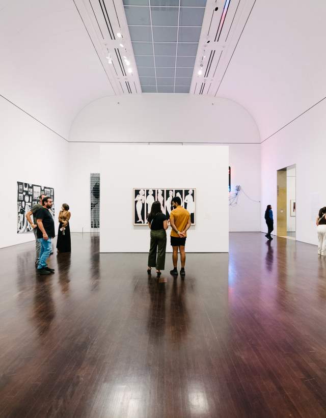 People admiring an art exhibit in a large white room at the Blanton Museum of Art.