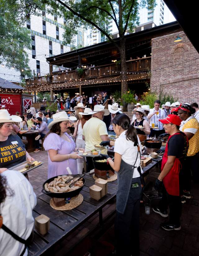 Attendees lined up for a buffet-style meal on the patio at Banger's with string lights above and staff helping serve