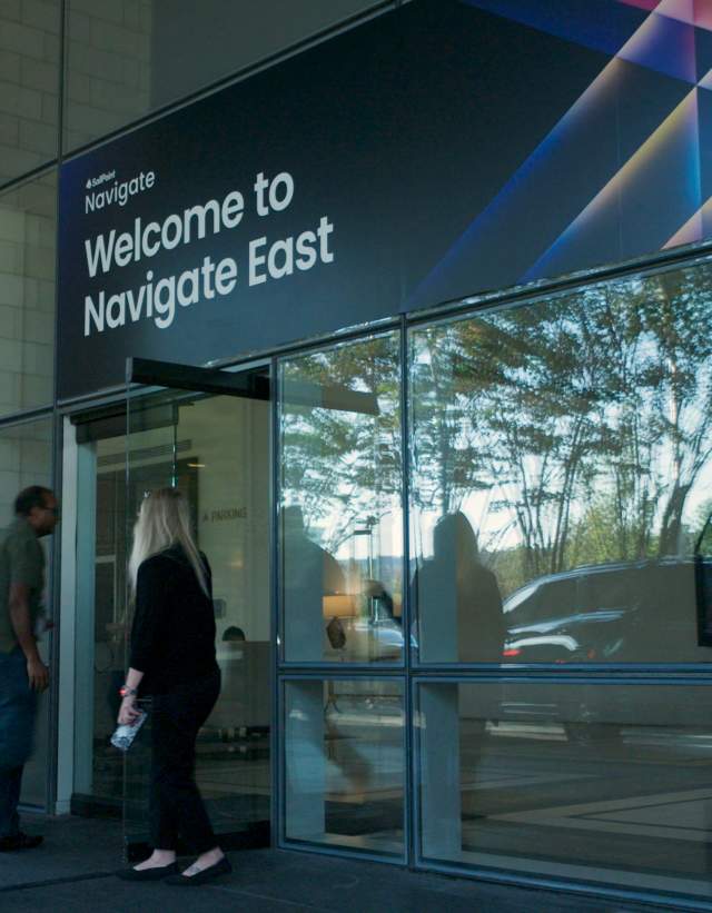 Man and woman walking into the glass doors under a sign that says Welcome to Navigate East.