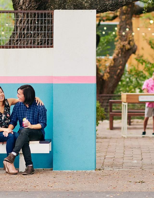 Couple sitting in front of Bienvenidos sign under live oak tree at Fresas outdoor patio in Austin Texas