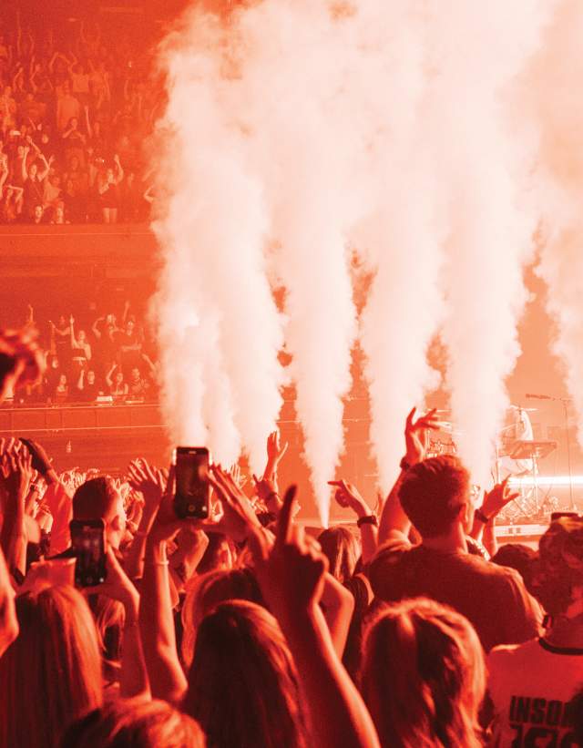 Photo from the audience looking up at the stage at ACL Live music venue. There are smoke machines at the front, and the room is tinged in red/orange light