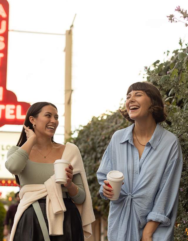 Two women walking and laughing on South Congress Avenue. Austin Motel neon sign is lit up in background