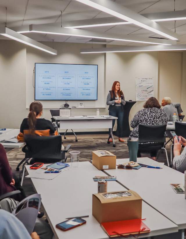 People gathered in a classroom setting, looking at a teacher at the front of the room.
