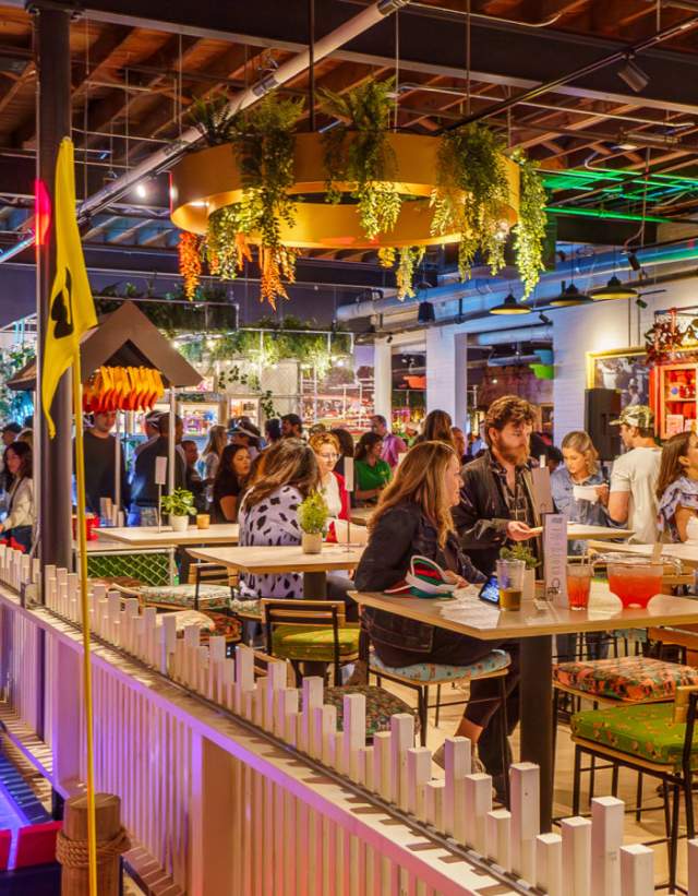 People sitting at bartop tables enjoying food and drink in the colorfully lit Holey Moley Golf Club.
