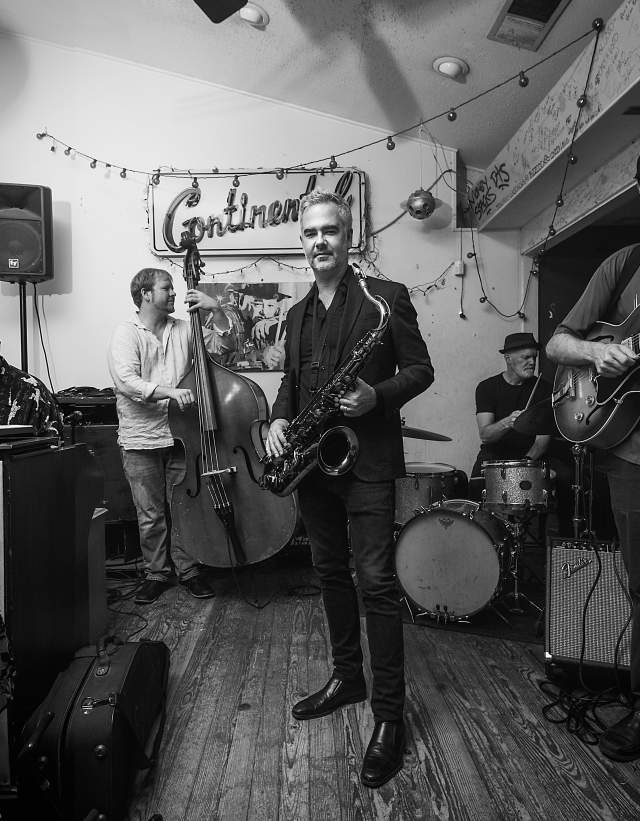Elias Haslanger holds saxophone in front of and band and Continental sign