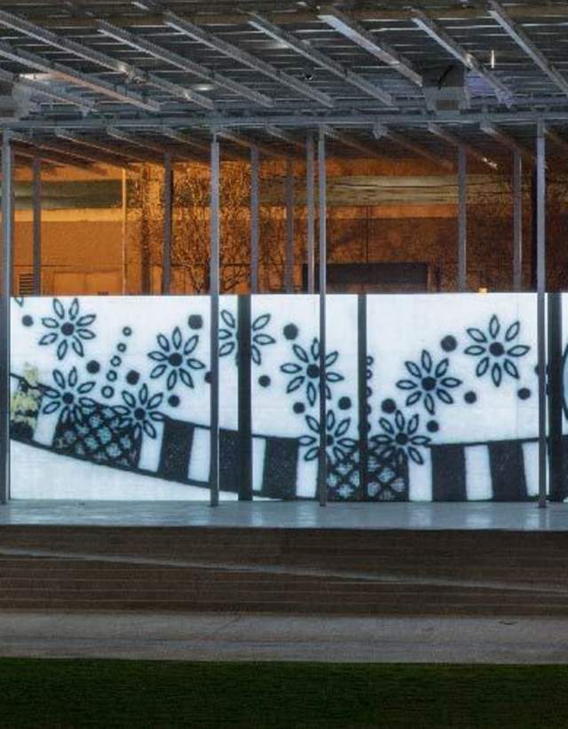 Person walking in the dark past an illuminated black and white mural featuring geographic shapes and a silhouetted face.