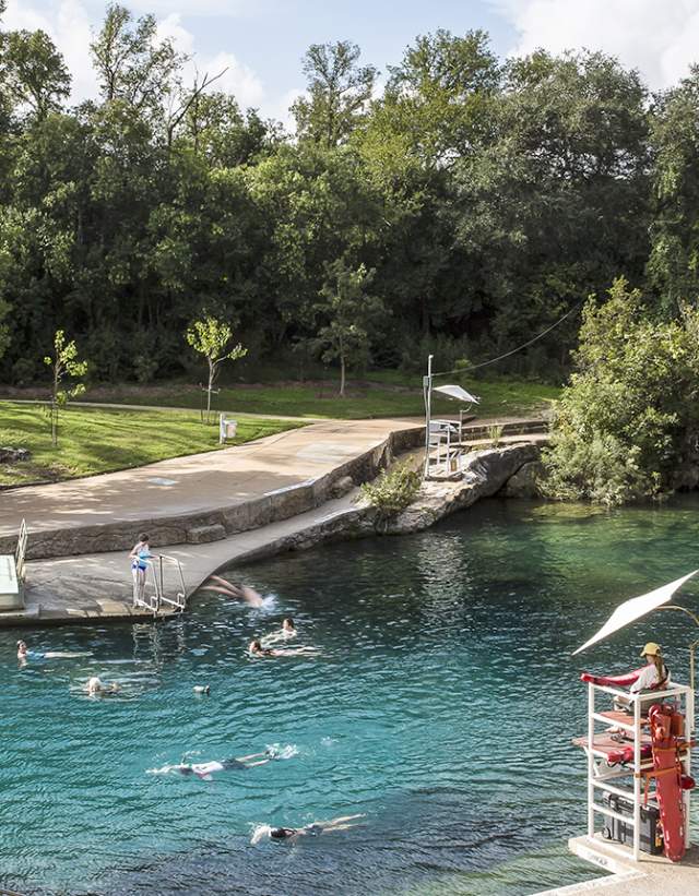 Historic Barton Springs Pool with several people swimming through the clear water and a lifeguard on duty