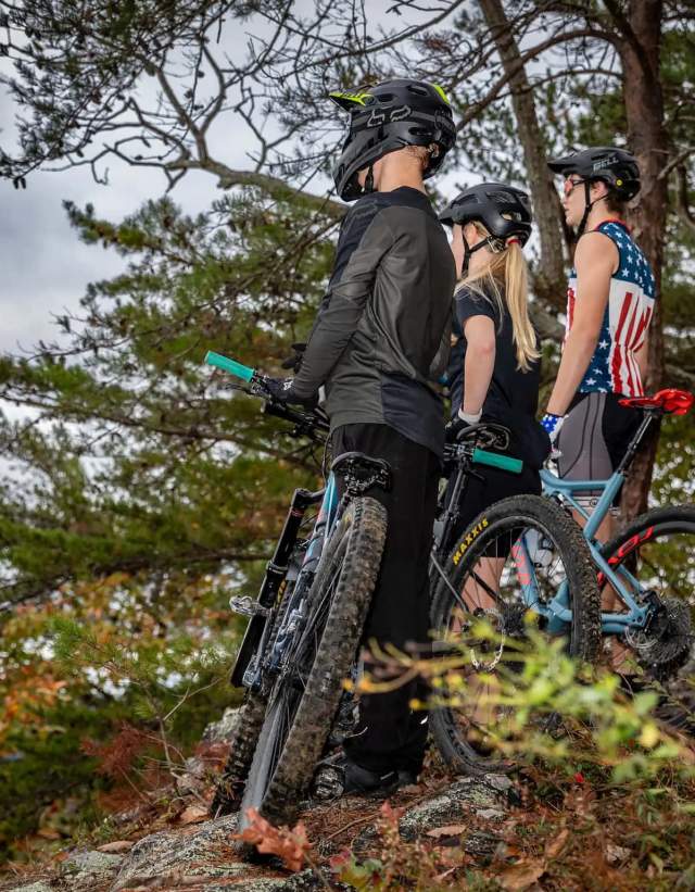 Three young mountain bikers stare out over the view of an overlook during a cloudy day at Double Oak Park. They each are standing next to their mountain bikes.