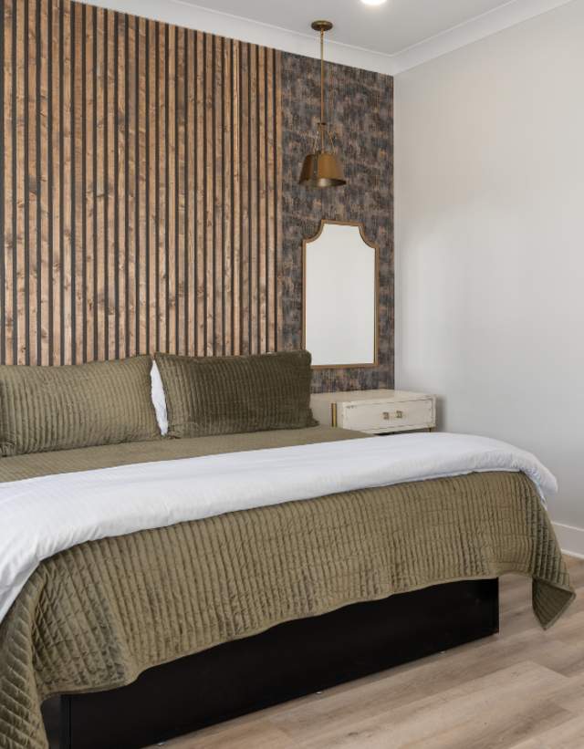 A modern hotel room with a wooden slat wall, a desk, and green bedding.