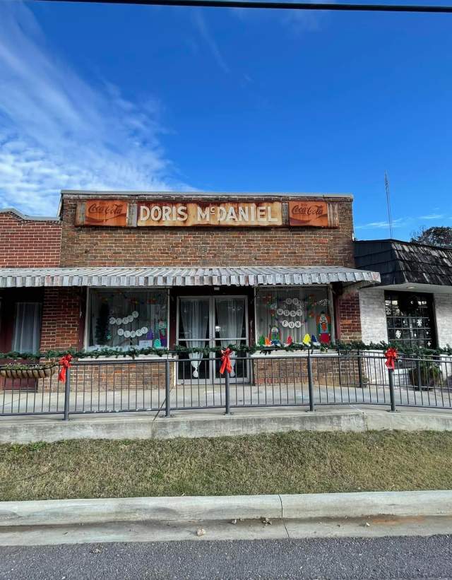Old brick building with a sign that says Doris McDaniel, decorated for Christmas with window paintings and garland with red bows on the railing