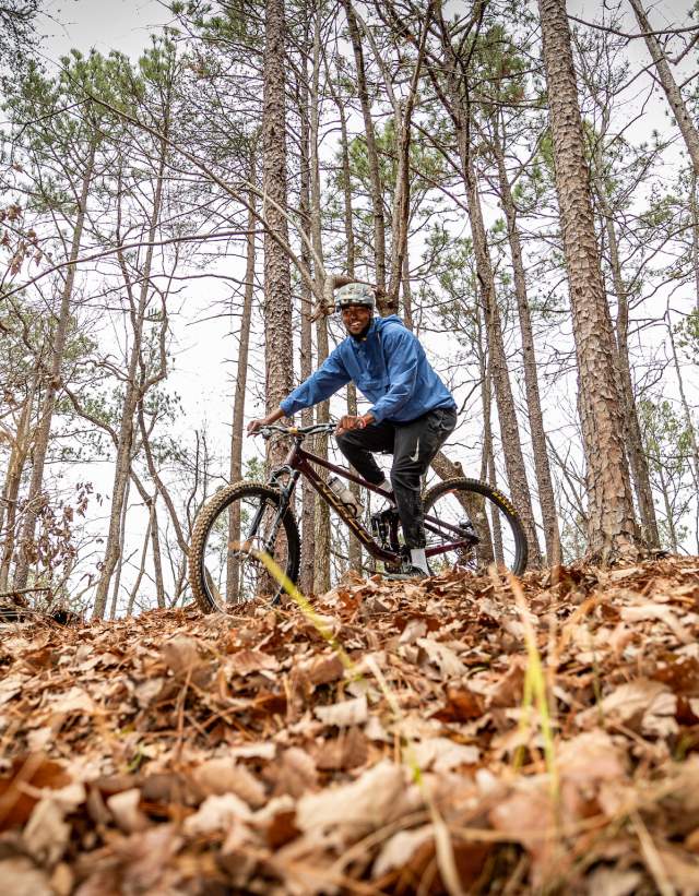 A mountain biker rides on a trail full of crunchy brown leaves.
