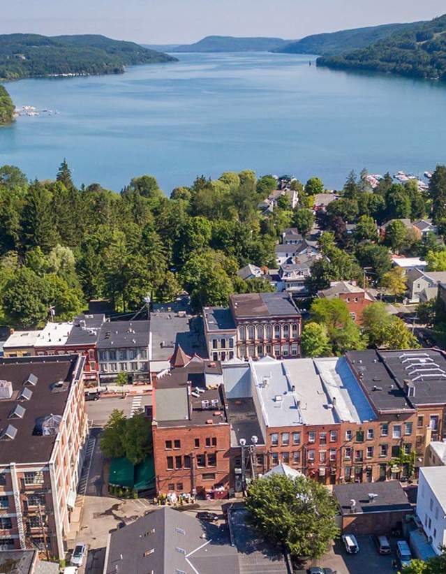 An aerial photo of Cooperstown with main street buildings in the foreground and a lake and wooded areas in the background.