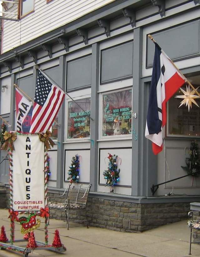 A gray and white store facade with open flags, an American flag, and a sign that says antiques.