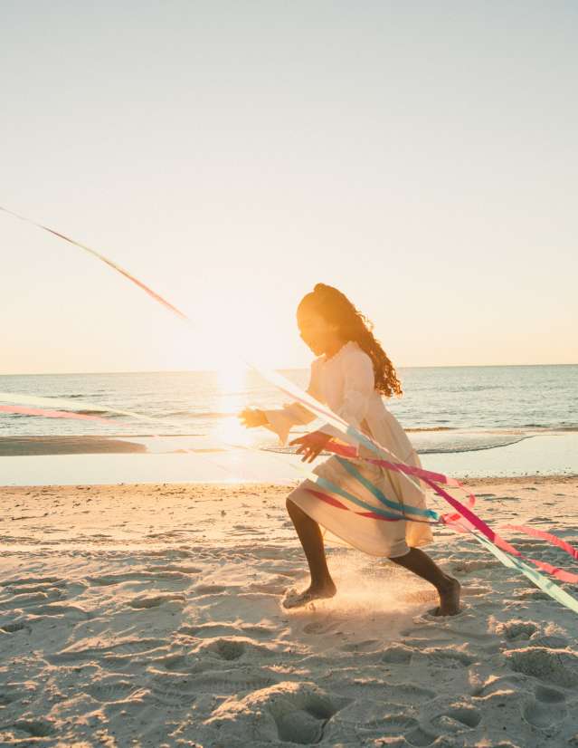 A little girl runs along the shoreline of Cape San Blas chasing a kite as ribbons stream down from the kite.