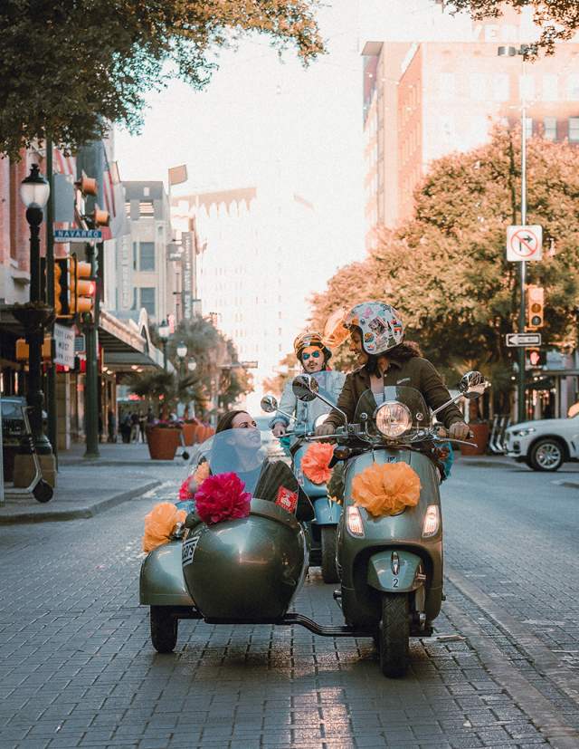 Woman driving vespa with passenger in side car in San Antonio, Texas.