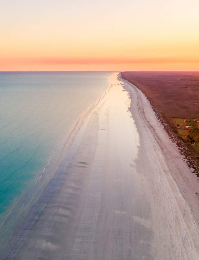 An aerial view of 80 Mile Beach showing the ocean, beach and caravan park at sunrise