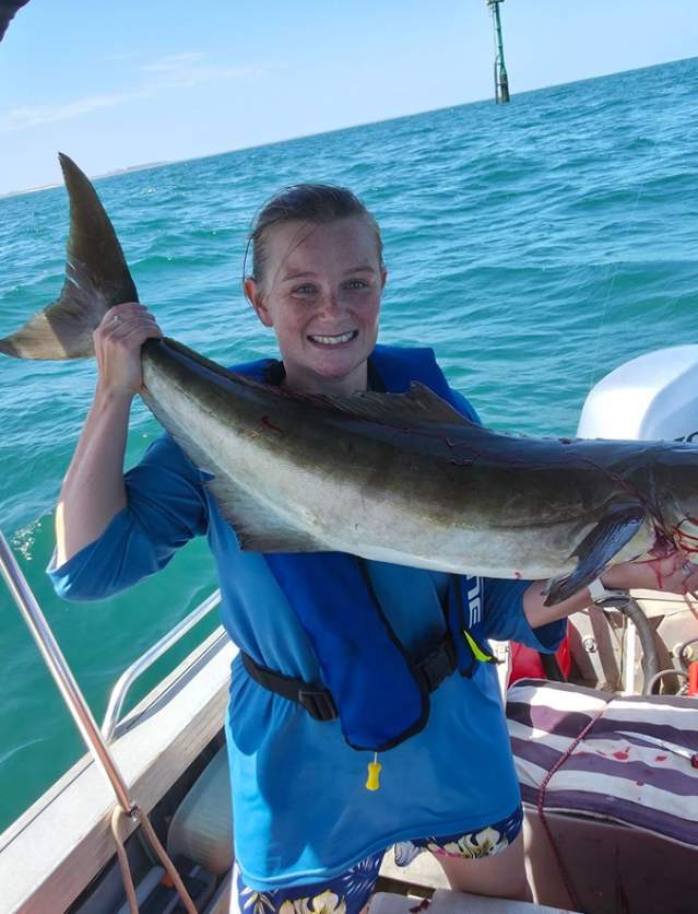 A woman in a boat holding a freshly caught cobia fish, in the waters off Port Hedland
