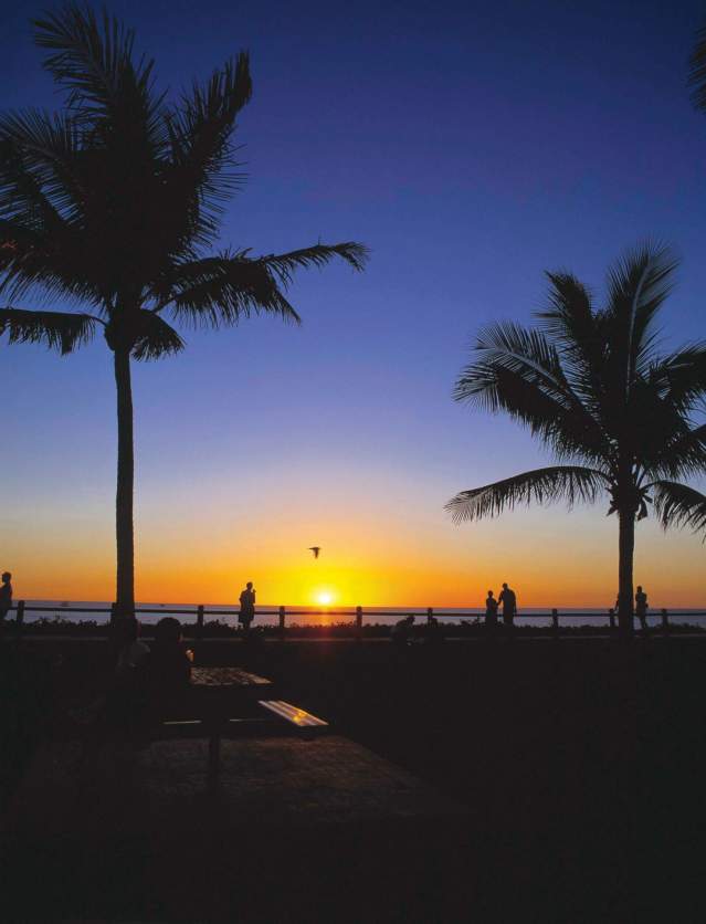 Sun setting over the ocean at Cable Beach in Broome, with people and palm trees silhouetted in the light