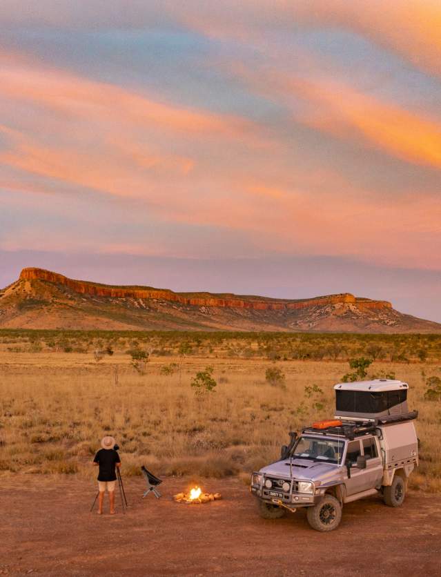 A car parked with a man taking a photo of the Cockburn Ranges in the background. Image taken at sunset.