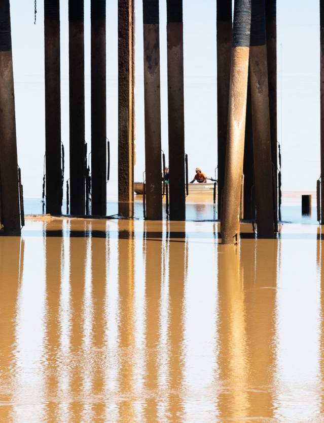 A view of the pylons at Derby Jetty with a boat in the background and reflections on the water