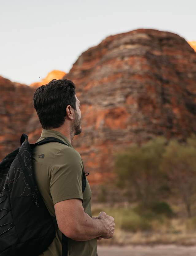 A man stands on a walking track, looking up at the striped domes of the Bungle Bungle Range, Purnululu National Park
