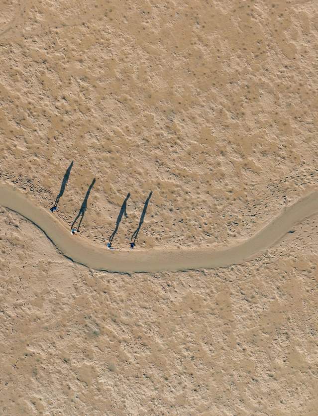 Aerial shot of a tour group walking along the tidal flats, their shadows silhouetted against the sand