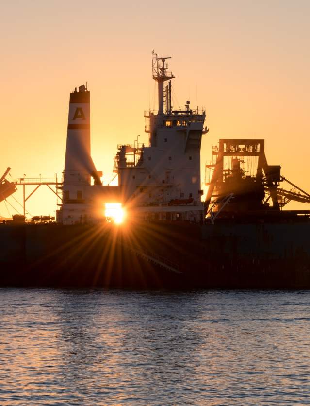 Sun setting behind large ships in port at the Port of Port Hedland