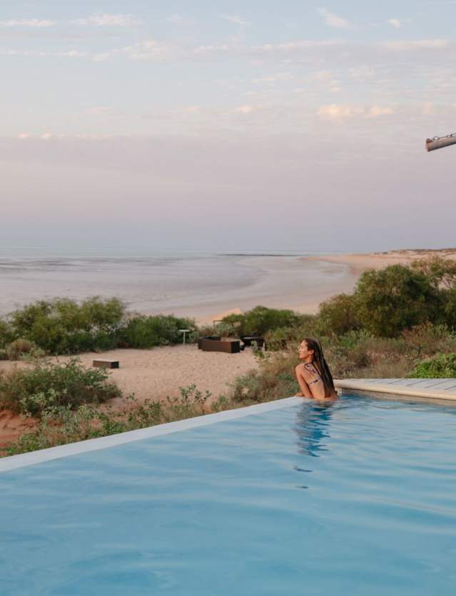 View from the swimming pool at Eco Beach Wilderness Retreat across the Indian Ocean. A woman is in the pool, looking at the view