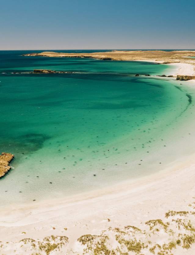 Taken from a vantage point higher than the beach, the image shows the beach, clear waters and True North at anchor on one of the Montebello Islands