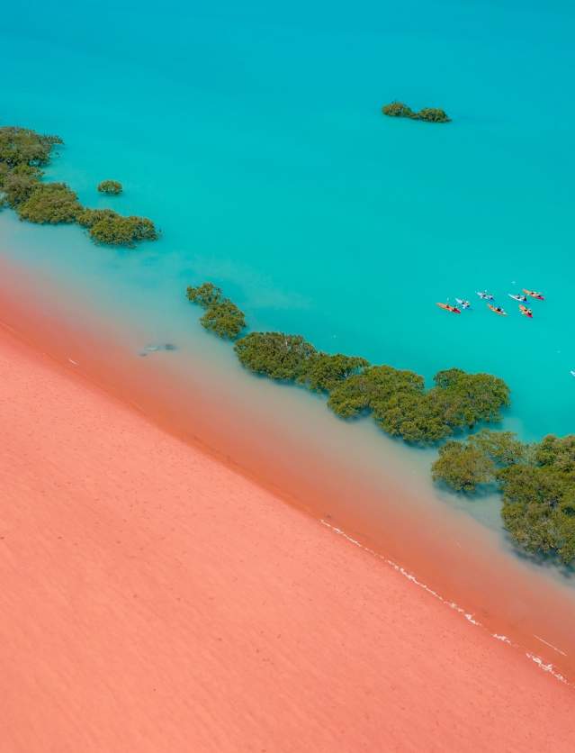 An aerial view of kayakers in Roebuck Bay, Broome showing turquoise waters and red sands