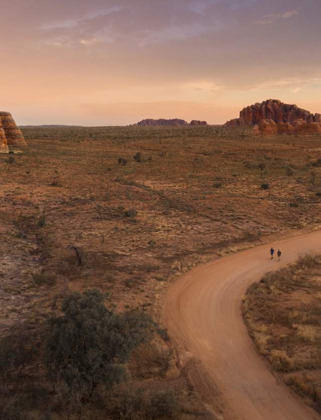 Two people walking on a track near the Bungle Bungle domes at sunset.